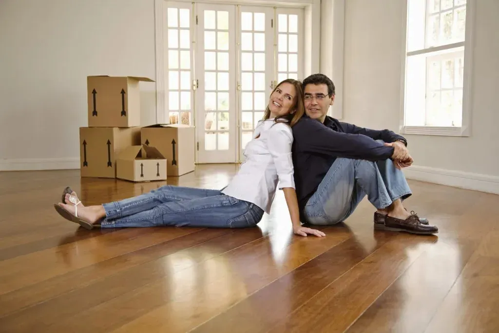 Couple sitting back-to-back on floor beside moving boxes