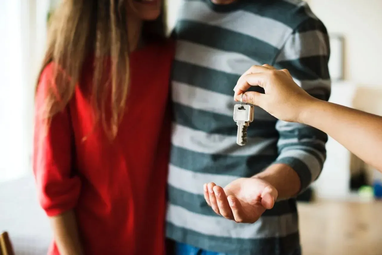 Hand passing house keys to smiling young couple