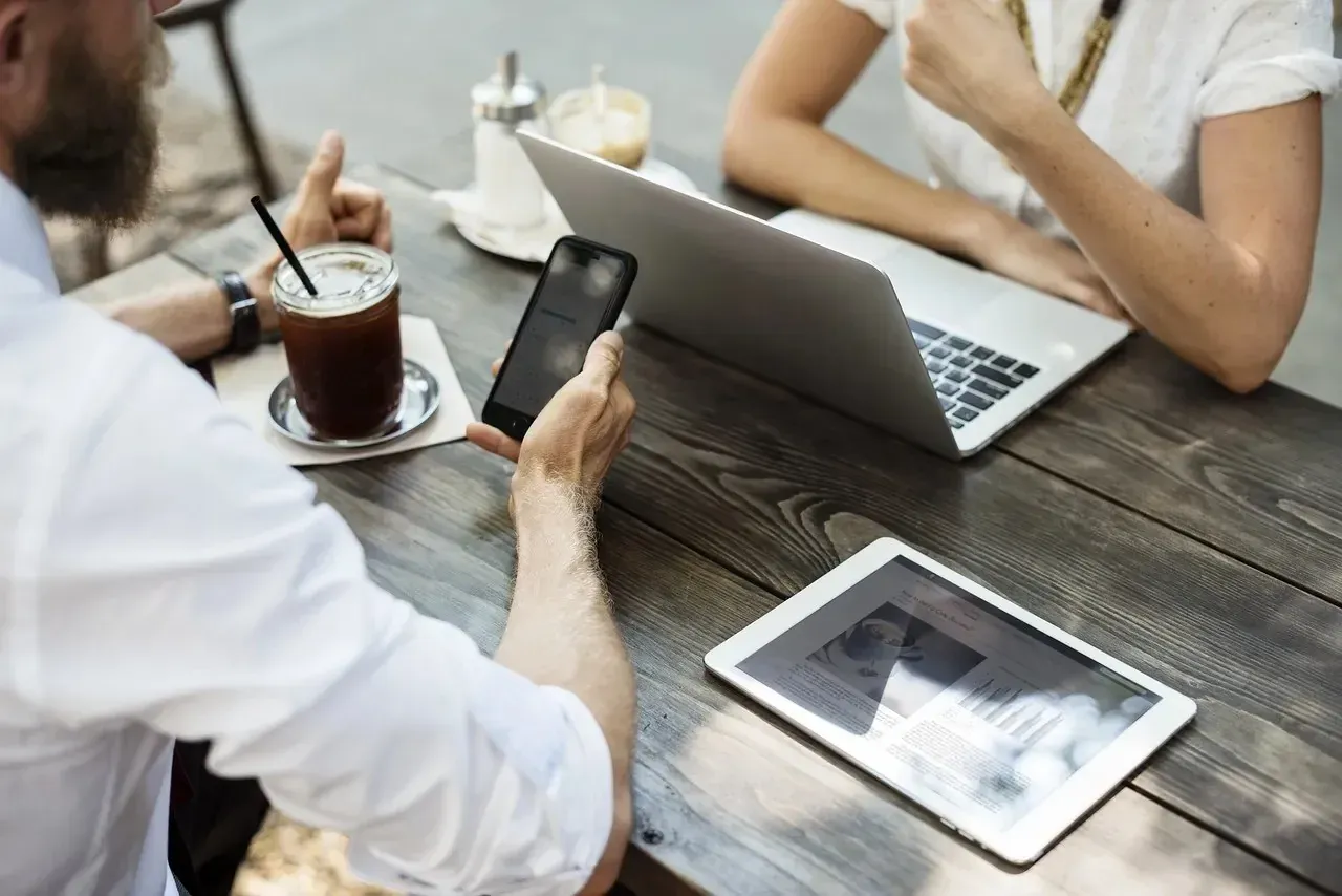Two people with laptop, phone and tablet at outdoor table