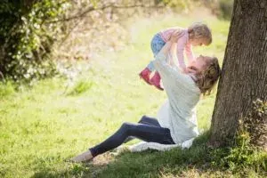 Mother lifting child under tree