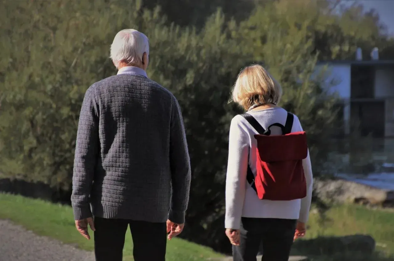 Senior couple with red backpack walking outdoors, rear view