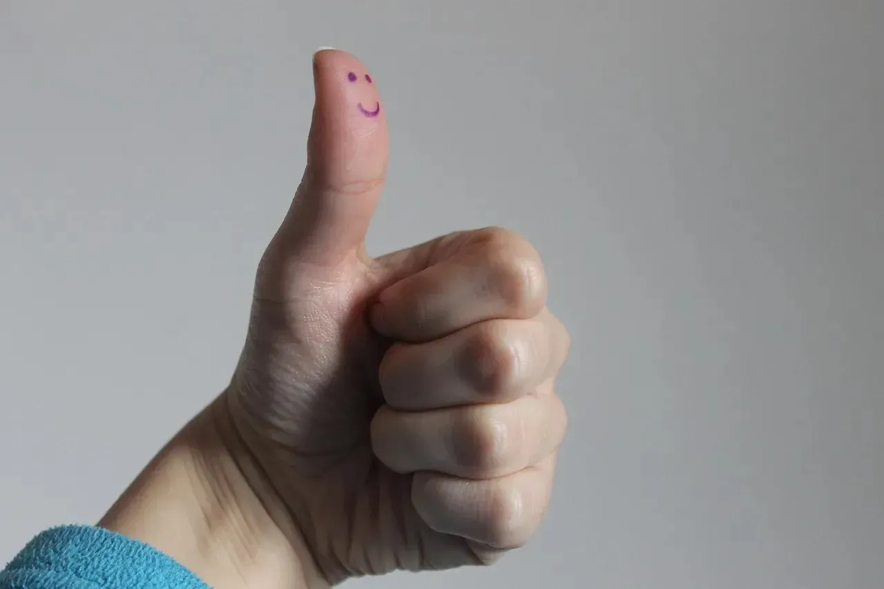 Thumbs-up hand with smiley face drawn on thumb