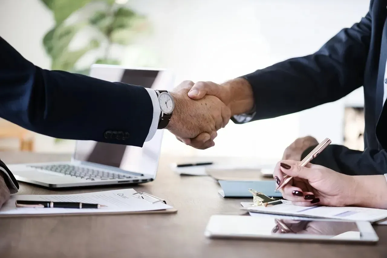 Business handshake over desk with laptop and documents