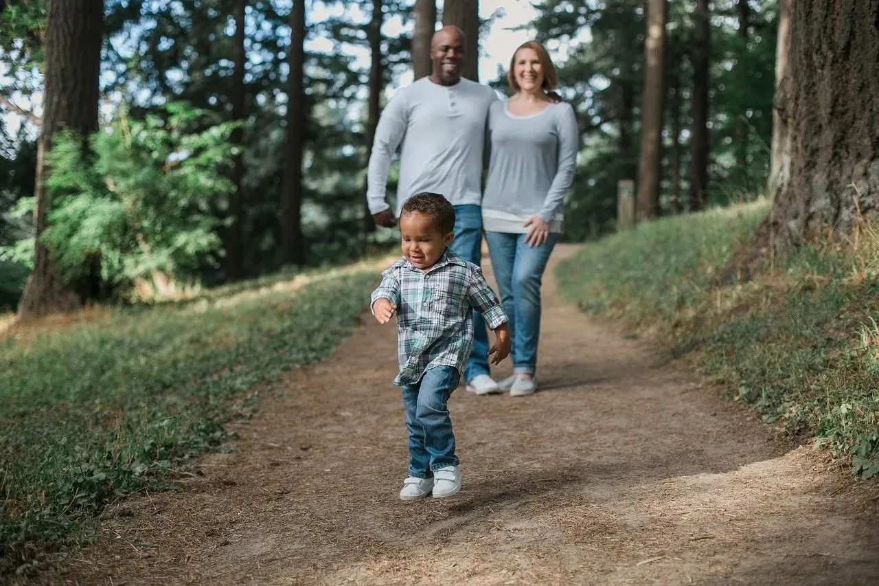 Parents watching toddler walk on forest path