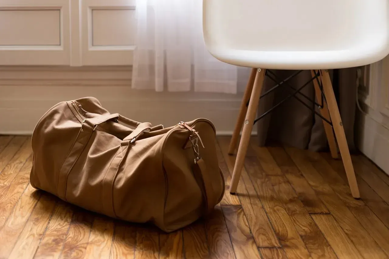 Brown duffel bag on wooden floor beside chair