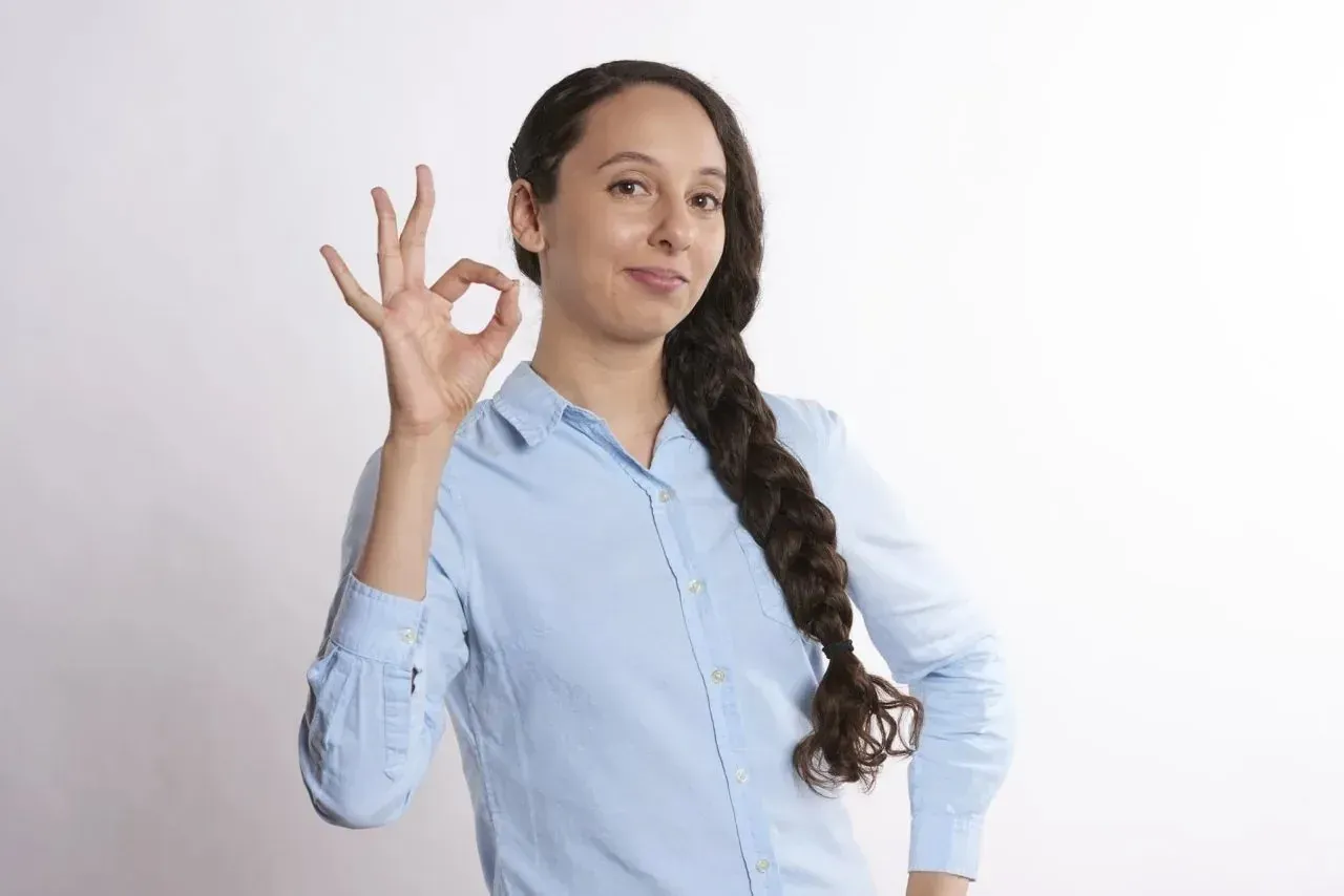 Smiling woman in blue shirt giving OK sign