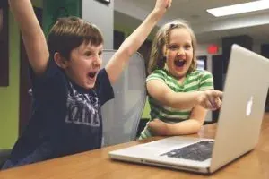 Two excited kids cheering at laptop