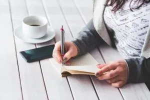 Woman writing in notebook, coffee