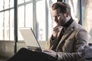 Man in coat using laptop pensively