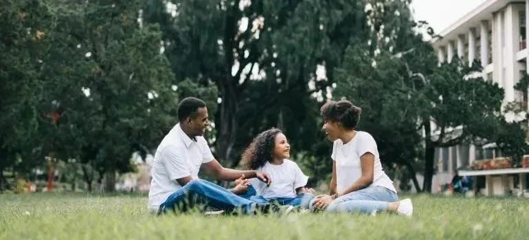 Parents and young daughter sitting on park grass