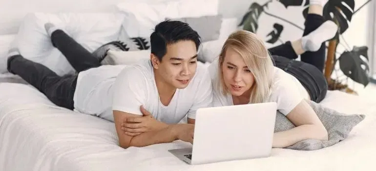 Couple lying on bed browsing laptop together