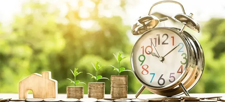 Alarm clock, coin stacks with sprouts, wooden house cutout