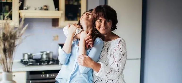 Mother hugging adult daughter in home kitchen
