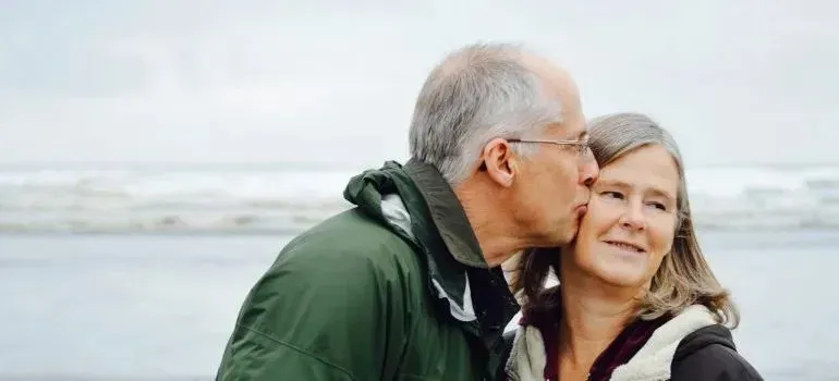 Senior man kissing smiling woman's cheek by the sea