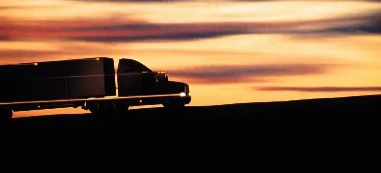 Semi-truck silhouette against orange sunset sky, no markings visible