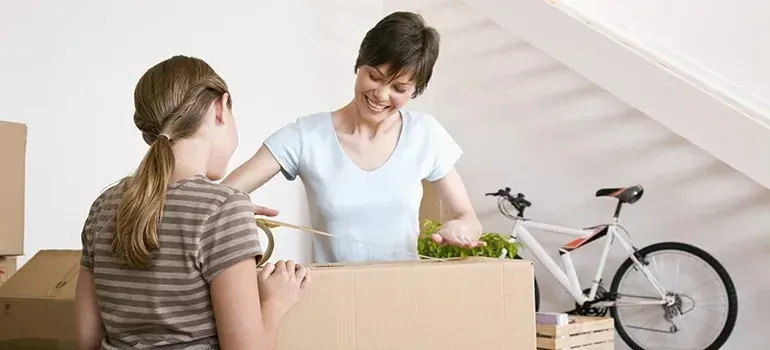 Mother and daughter taping cardboard moving box indoors