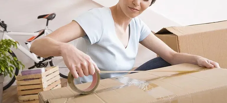 Woman sealing cardboard moving box with packing tape