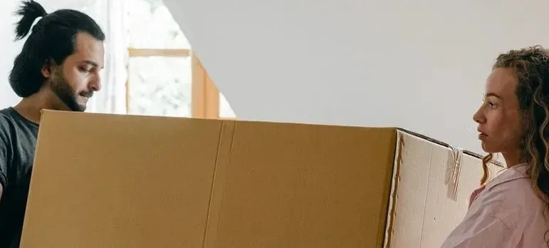 Couple carrying large plain cardboard box together indoors