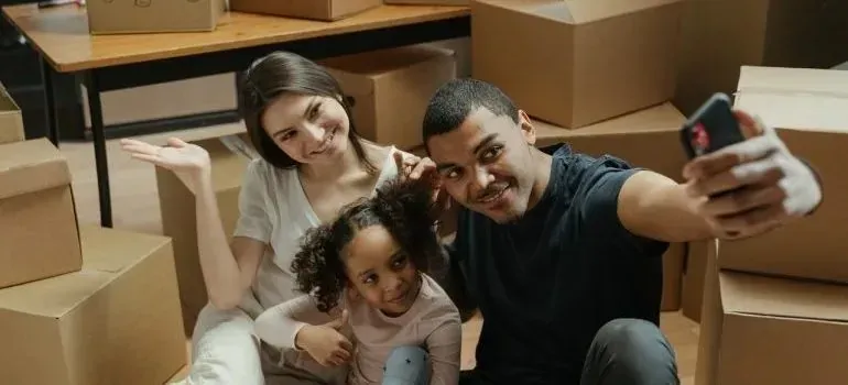 Family taking phone selfie surrounded by moving boxes