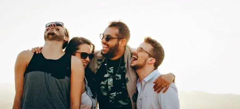 Four friends in sunglasses laughing together outdoors