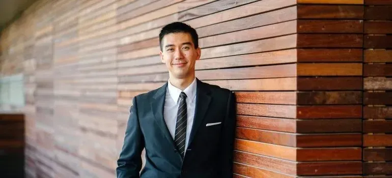 Smiling young man in suit leaning against wooden wall