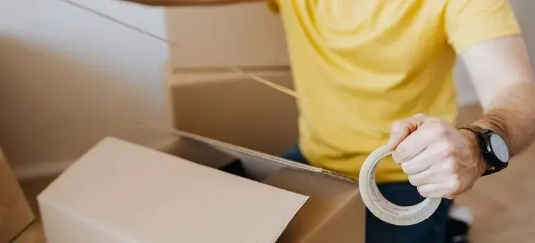 Man in yellow shirt taping cardboard moving box
