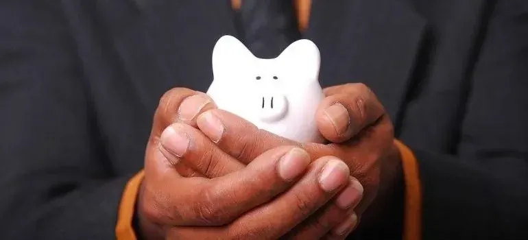 Hands in suit cupping a white piggy bank