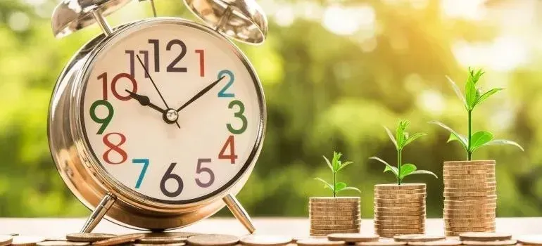 Alarm clock beside coin stacks with sprouting plants