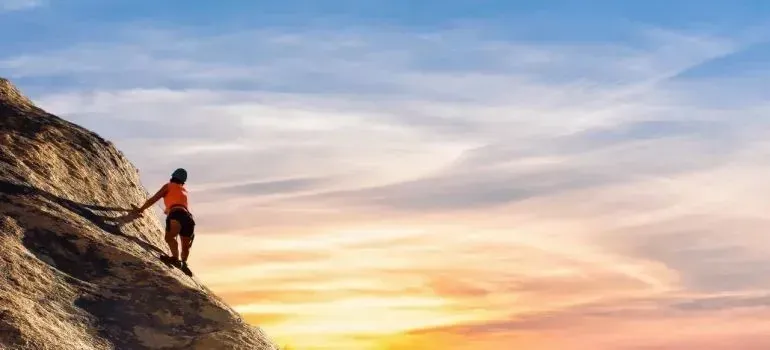 Climber in orange shirt scaling rock at sunset