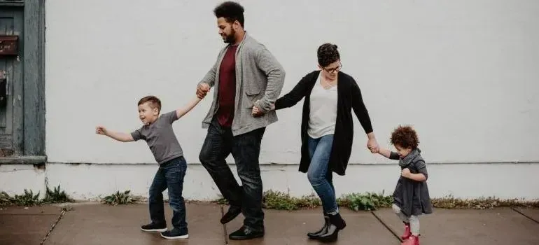 Family of four holding hands walking past white wall
