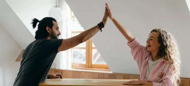 Couple high-fiving over cardboard box in attic apartment