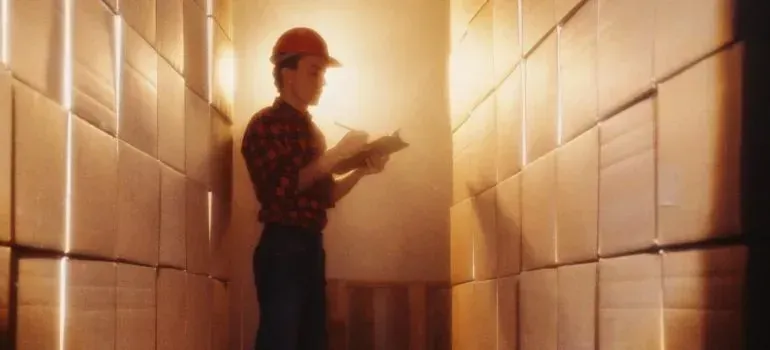 Worker in hard hat checking inventory between stacked boxes