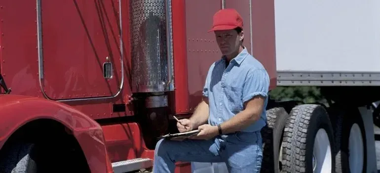 Driver with clipboard seated on unmarked red semi truck