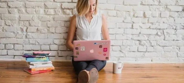 Woman using sticker-covered laptop against white brick wall