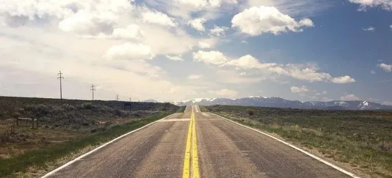 Straight rural highway toward snowy mountains, blue sky