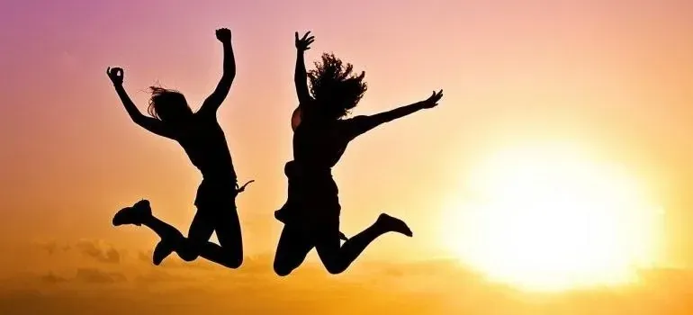 Two silhouetted people jumping joyfully against sunset