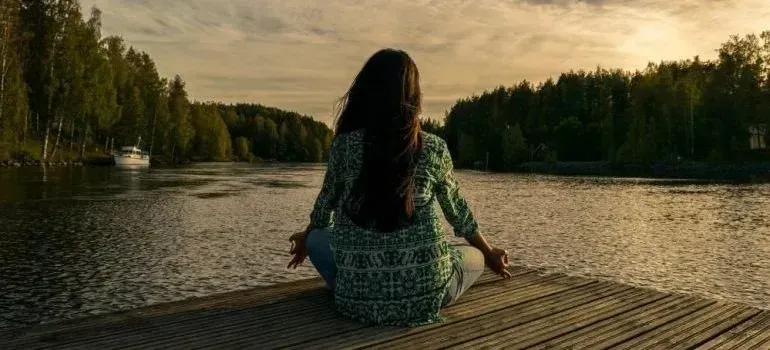 Woman meditating on lakeside dock at sunset