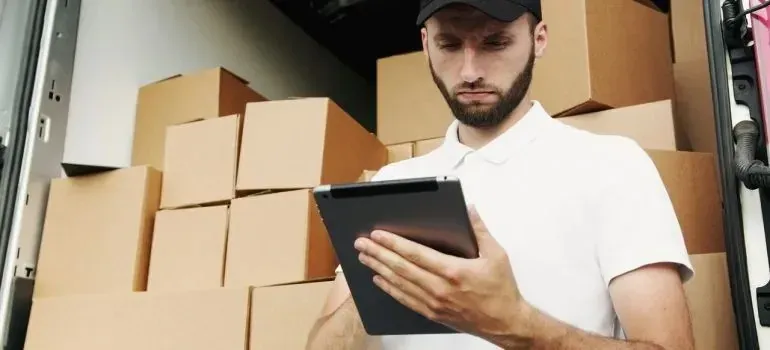 Courier in plain unbranded cap using tablet beside boxes in van