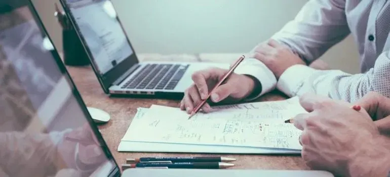 Two people reviewing paperwork with pens and laptops