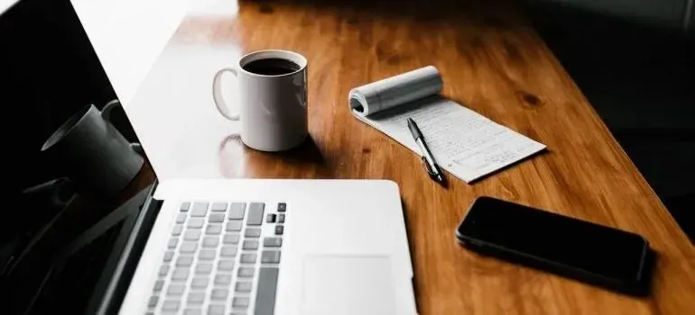 Laptop, coffee mug, notepad, and phone on wooden desk