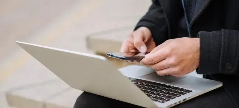 Person outdoors using smartphone over an open laptop