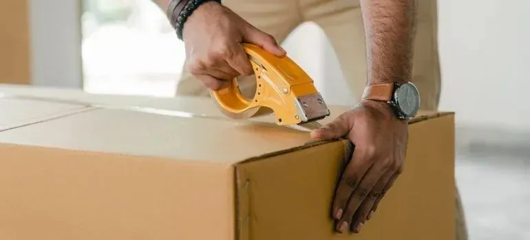 Man sealing cardboard box with yellow tape dispenser
