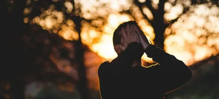 Silhouetted man covering his face with hands at sunset
