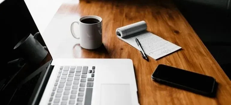 Laptop, coffee mug, notepad, and phone on wooden desk