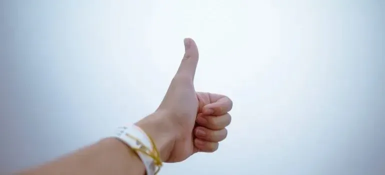 Hand giving thumbs-up against plain light background