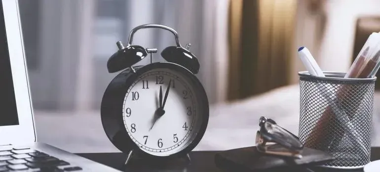 Black alarm clock on desk beside laptop and pens