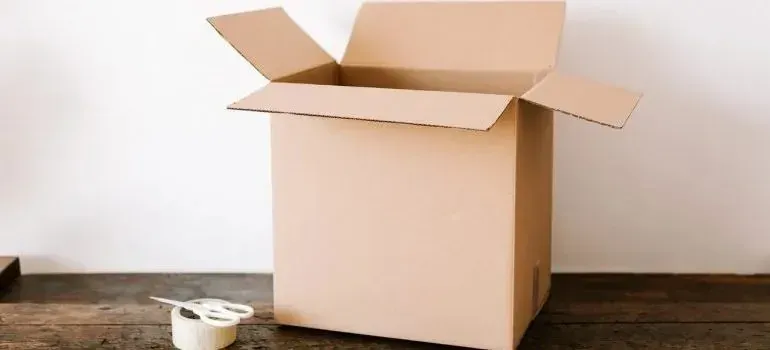 Open cardboard box and packing tape on wooden table