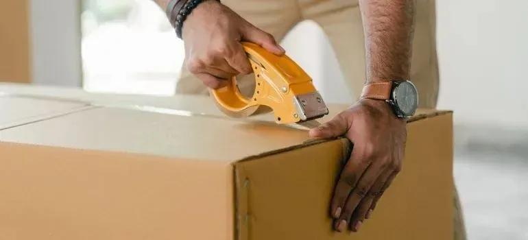 Man sealing cardboard box with yellow tape dispenser