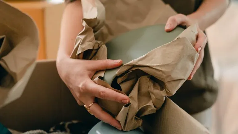 Hands wrapping green bowl in brown packing paper