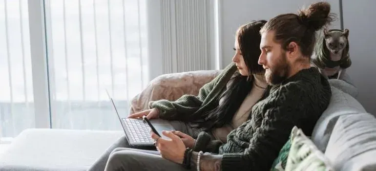 Couple on sofa browsing laptop with cat